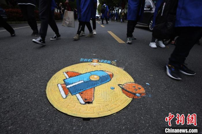 大学生们在校园主干道井盖上绘制航天图案。　泱波 摄